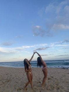 two women in bikinis on the beach reaching up to catch a frisbee