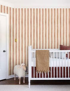 a baby's room with striped wallpaper and a sheep statue in the foreground