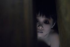 a young child is hiding in the corner of a dark room with his eyes wide open