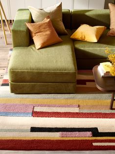 a green couch sitting on top of a wooden floor next to a table with flowers