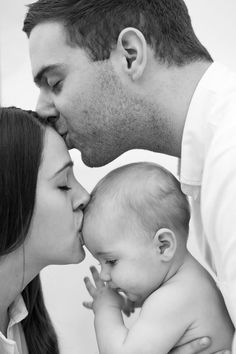 a man and woman kissing their baby while he is holding the baby's head