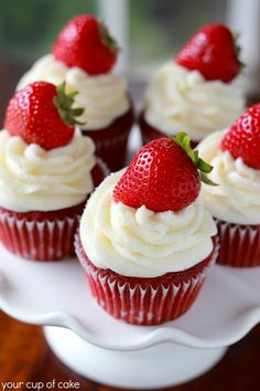 cupcakes with white frosting and strawberries on top are arranged on a plate