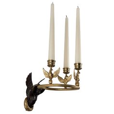 a candle holder with three candles and a bird figurine hanging from it's side