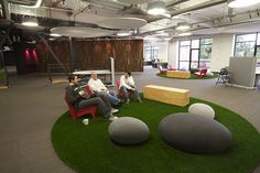 three people sitting on chairs in an office with artificial grass and fake rocks around them