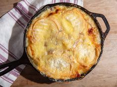 an old cast iron skillet filled with food on top of a wooden table next to a white and pink towel