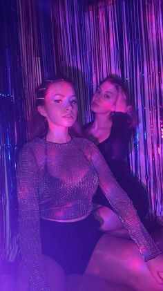 two women are posing in front of purple lights