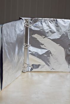 an open silver binder sitting on top of a white table next to a wall