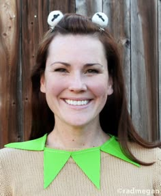 a woman with two birds on her head wearing a green sweater and smiling at the camera