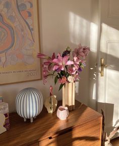 a vase filled with pink flowers sitting on top of a wooden dresser next to a painting