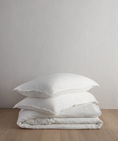 three pillows stacked on top of each other in front of a white wall and wooden floor