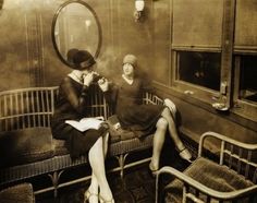 two women sitting on benches in an old train car, one is talking on the phone