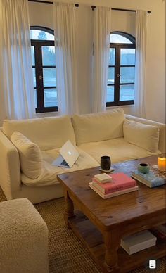 a living room with couches, coffee table and two windows in front of them