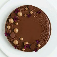 a chocolate cake on a white plate with purple flowers and nuts around the edges, ready to be eaten