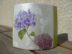 a vase with purple flowers painted on it sitting on a wooden table next to a wall