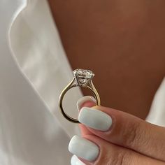 a woman's hand holding a ring with a diamond on it and white nail polish