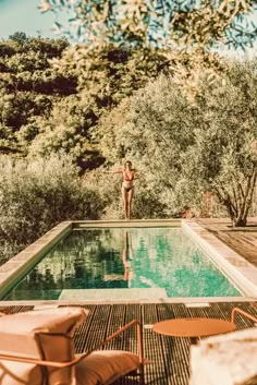 a woman standing in front of a pool surrounded by trees