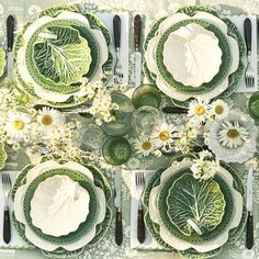 a table set with plates, silverware and green floral napkins on top of it