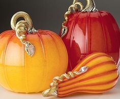 two orange pumpkins sitting next to each other on a white surface with gold accents