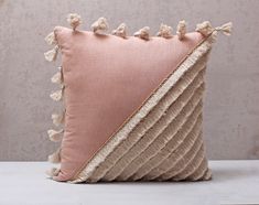 a pink and beige pillow with tassels on the bottom, sitting on a white table