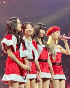 the girls are singing on stage with microphones in their hands and wearing santa costumes