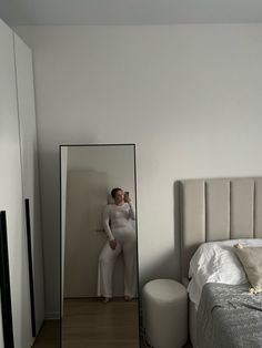 a woman standing in front of a mirror next to a bed