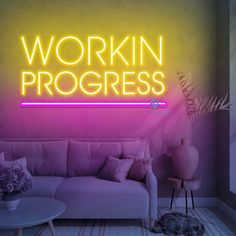 a neon sign that reads workin'progress in front of a couch and coffee table