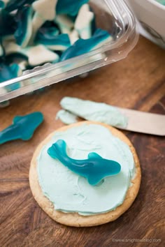 a cookie with blue icing sitting on top of a wooden table next to a plastic container