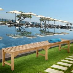 a wooden bench sitting on top of a lush green field next to a swimming pool