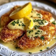 a white plate topped with fried chicken covered in gravy and lemon wedges