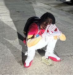 a young man sitting on the ground with a teddy bear in his lap and wearing sneakers