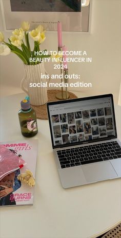 an open laptop computer sitting on top of a white table next to a vase with flowers