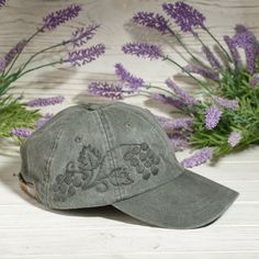 a gray hat sitting on top of a wooden table next to purple flowers and greenery