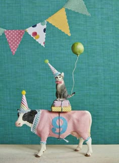 a toy cow with a birthday hat on it's head and some balloons in the air