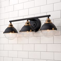 three lights are on the wall in front of a white brick wall with black and gold fixtures