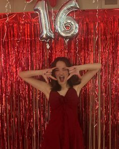 a woman standing in front of a red curtain with her hands on her head and the number 16 above her head