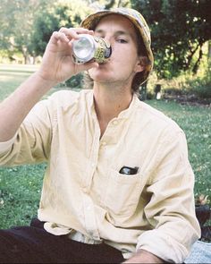 a man sitting in the grass drinking from a can with his eyes closed and mouth wide open