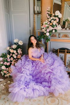 a woman in a purple dress sitting on the floor next to flowers and a mirror