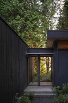 a house in the woods surrounded by trees and bushes with its doors open to let in light