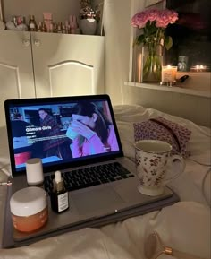 a laptop computer sitting on top of a bed next to a cup and saucer