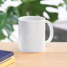 a white coffee mug sitting on top of a wooden table next to a blue book