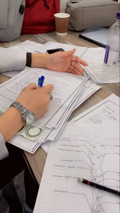 two people sitting at a table with papers and pens on top of them, one person is writing