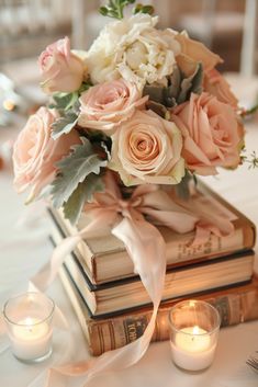 a bouquet of flowers sitting on top of two books with candles in front of them