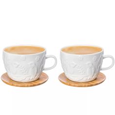 two white cups sitting on top of wooden coasters next to each other with designs