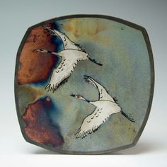 two birds are flying in the sky on a square glass object with an orange and blue background