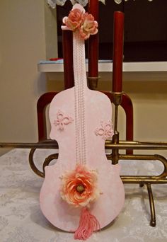 a pink violin with flowers on it sitting on a table next to two candles and a mirror