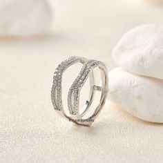 a white gold and diamond ring sitting on top of a table next to some rocks