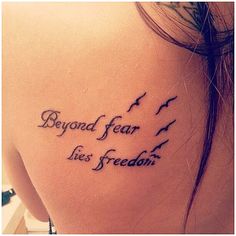 the back of a woman's shoulder with a tattoo saying, beyond fear lies freedom