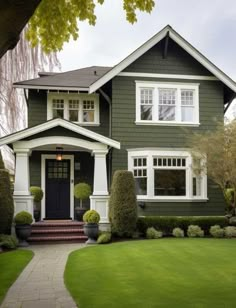 a green house with white trim on the front and side windows, trimmed in grass