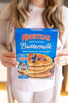 a woman holding up a box of buttermik with blueberries and strawberries on top