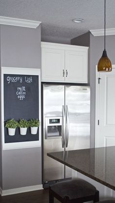 a kitchen with white cabinets and stainless steel refrigerator freezer next to a blackboard that says grocery list on it